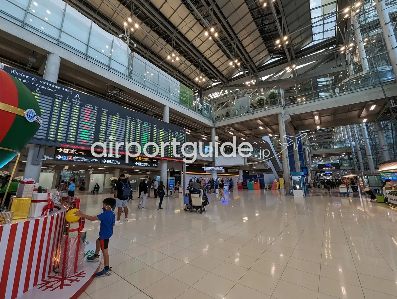 スワンナプーム空港の国内線到着階。「Domestic Arrivals Door A」の大型フライト案内板とAOTロゴ、下部に「Public Taxi／Airport Rail Link／Meeting Point」などの交通案内サイン、手前にクリスマス装飾。