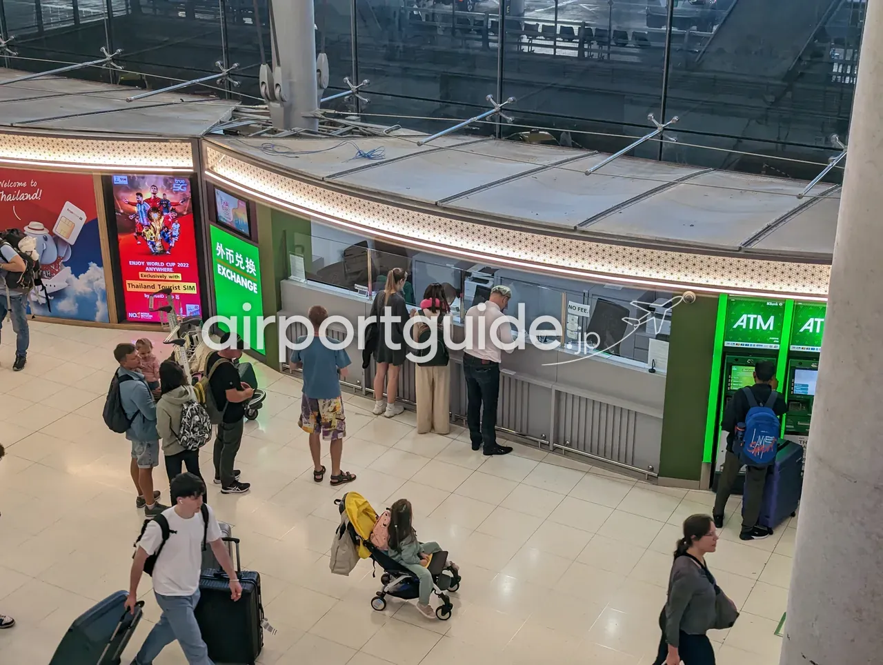 スワンナプーム空港・到着フロアの外貨両替カウンターとATMを上から見た様子。スーツケースを引いた大勢の旅行者が行き交う。