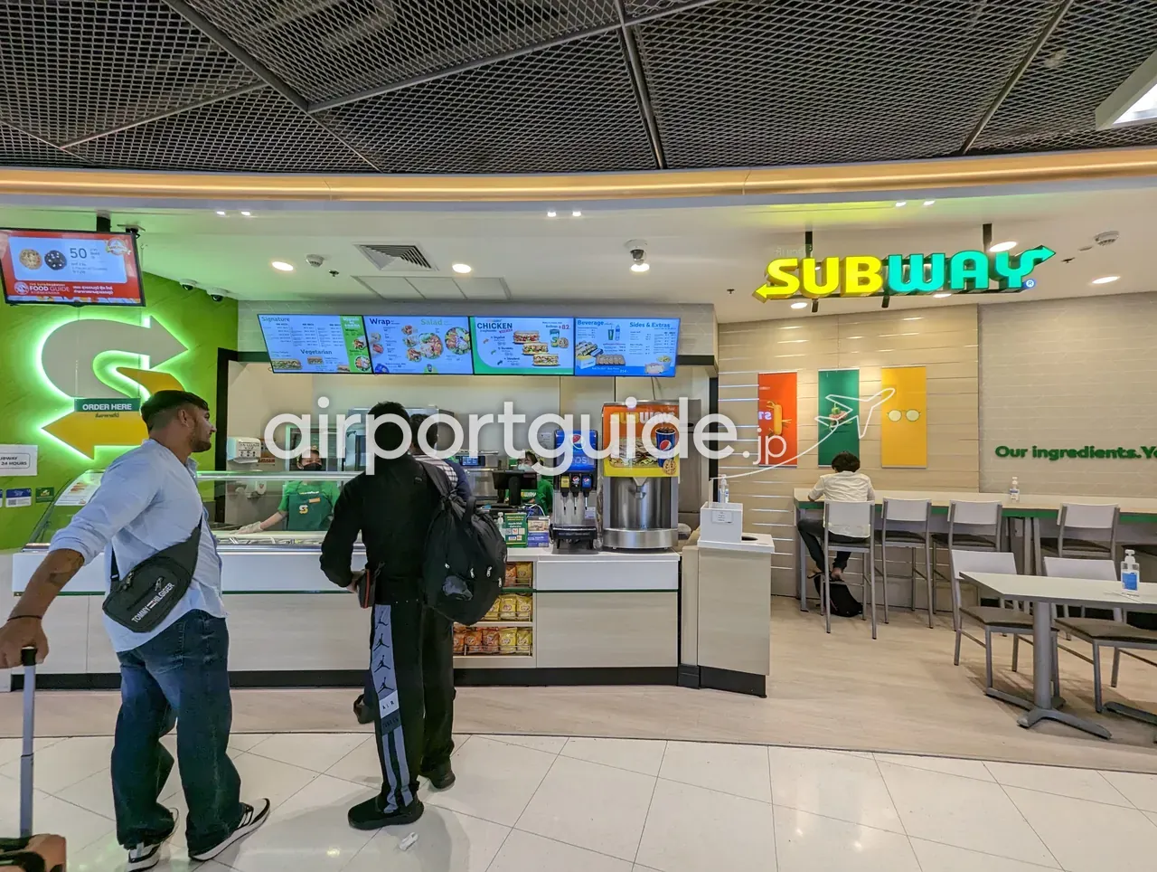 スワンナプーム空港内のサンドイッチ店「SUBWAY」。緑の看板と写真メニュー、「24 HOURS」の表示、カウンターで注文する旅客と奥のカウンター席。