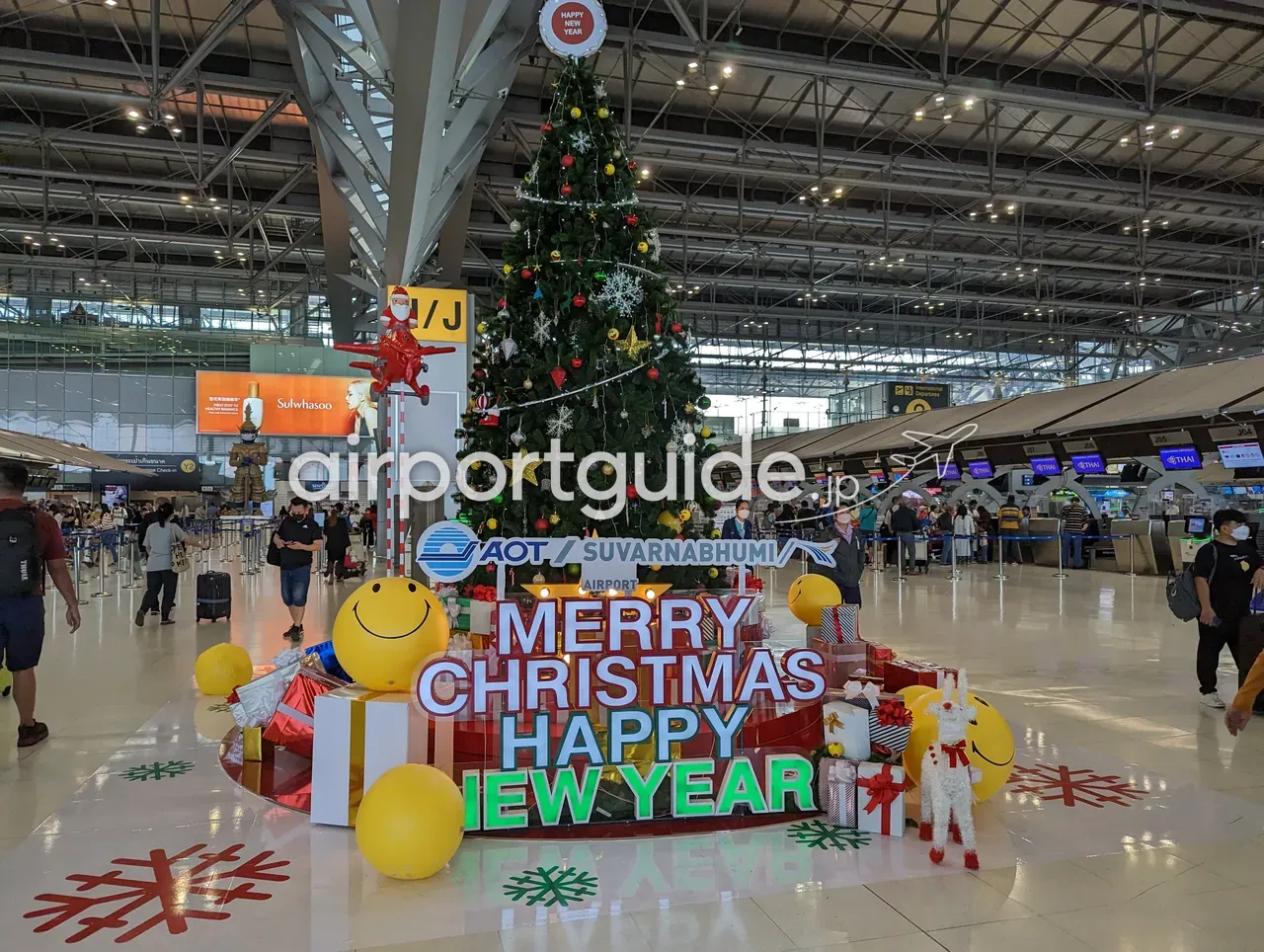 スワンナプーム空港の出発チェックインホールの大型クリスマスツリー。「AOT／SUVARNABHUMI AIRPORT」ロゴと「MERRY CHRISTMAS HAPPY NEW YEAR」の電飾、奥にTHAI（タイ国際航空）のチェックインカウンター。