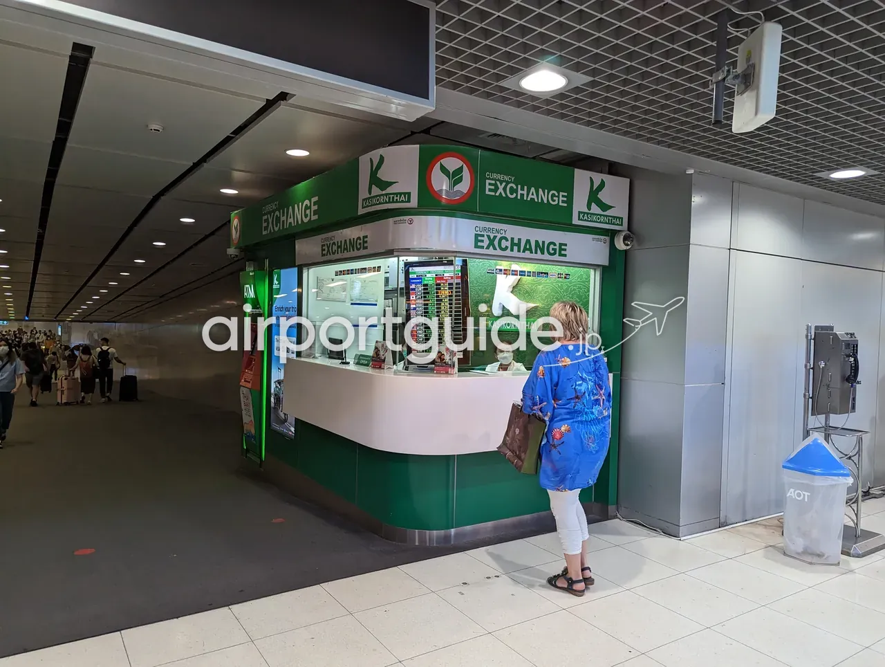 スワンナプーム空港・レールリンク（ARL）階のカシコン銀行（KBank）外貨両替ブースで、女性客がカウンターで両替の手続きをしている。
