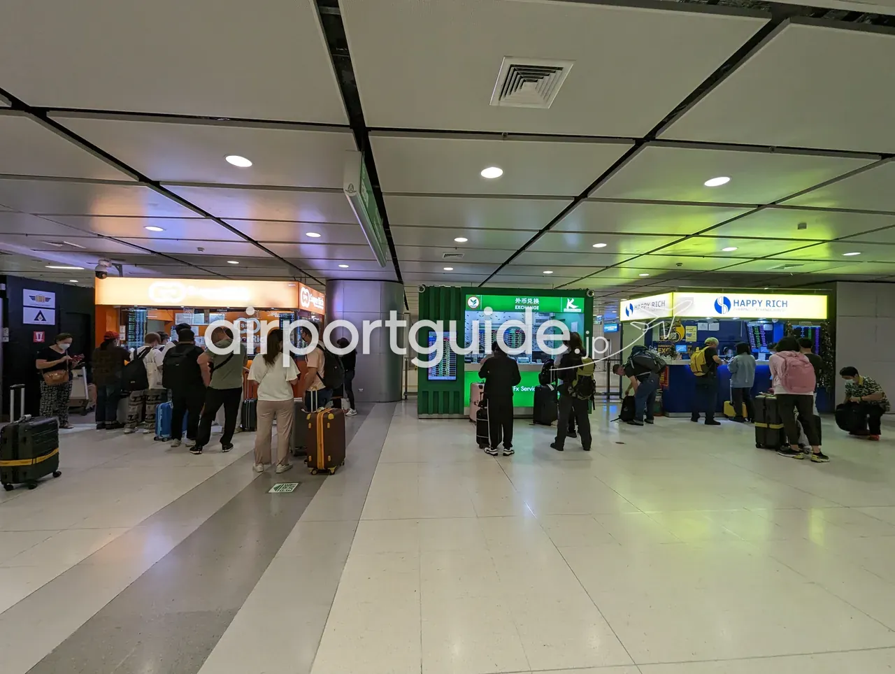 スワンナプーム空港・レールリンク階に並ぶ外貨両替ブース。オレンジのSuperRich、緑のカシコン銀行「外币兑换 EXCHANGE」、青と黄のHAPPY RICHのカウンターに、スーツケースの旅行者が並ぶ。