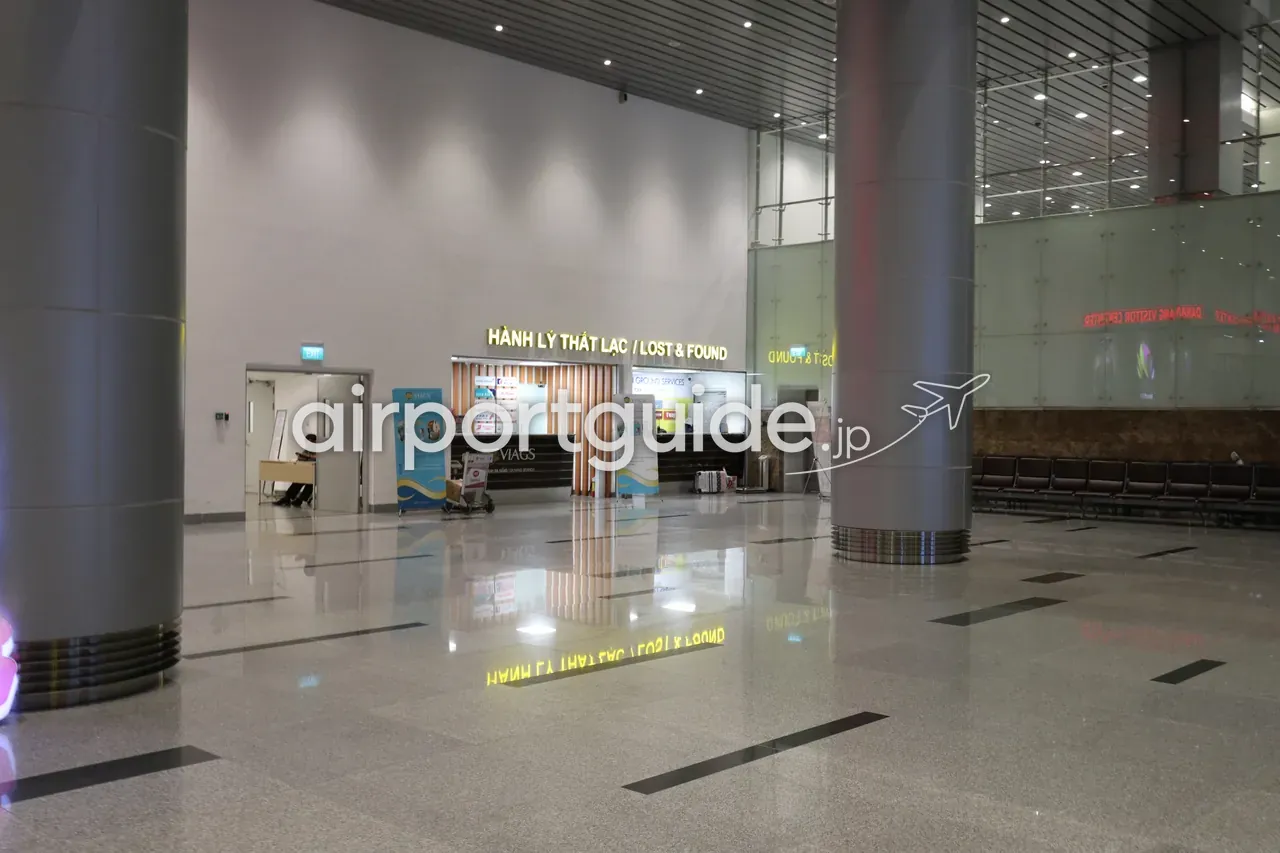ダナン国際空港の遺失物取扱（Lost & Found）カウンター。「HÀNH LÝ THẤT LẠC／LOST & FOUND」の黄色い表示と木ルーバーの受付、地上業務会社VIAGSの表示、脇に手荷物カートとベンチ。