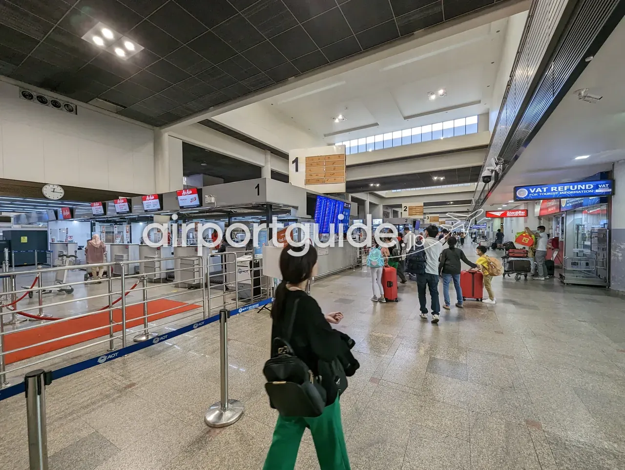 早朝のドンムアン空港出発階のチェックインエリア。カウンター番号「1」の島とエアアジアの赤い表示、「Fast & Easy」のセルフサービス案内、右手に「VAT REFUND FOR TOURIST INFORMATION」の青い看板、スーツケースを引く家族連れ。