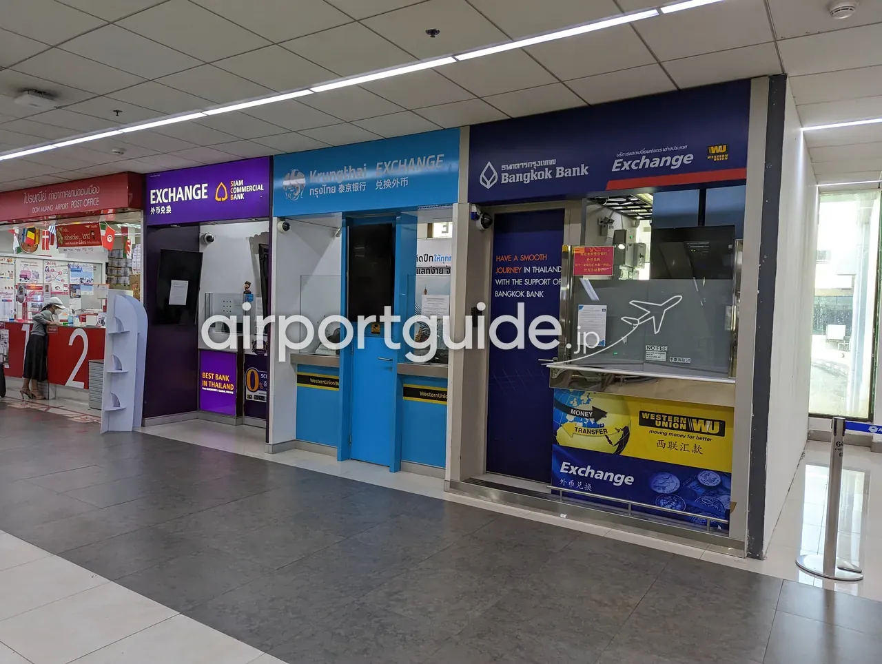 ドンムアン空港の通路に並ぶ両替所（SCB、Krungthai、Bangkok Bank）と、左端の赤い「DON MUANG AIRPORT POST OFFICE（郵便局）」の窓口。カウンターに「1」「2」の番号表示がある。
