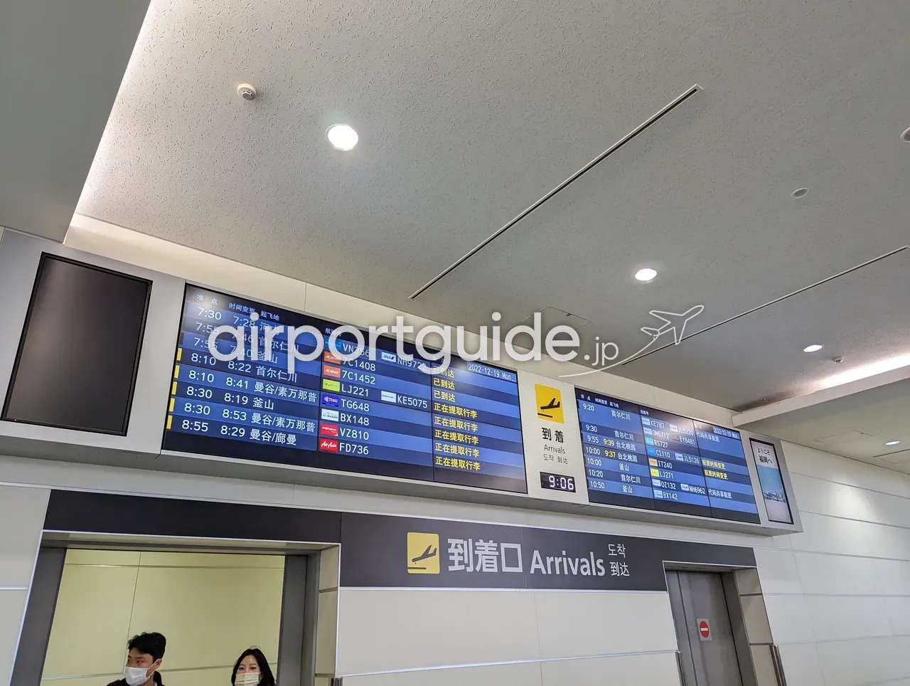 福岡空港国際線ターミナルの到着案内表示。「到着口 Arrivals」のサインの上に、河内（ハノイ）・ソウル仁川・釜山・バンコク・台北などの到着便の状況が多言語で表示されている。