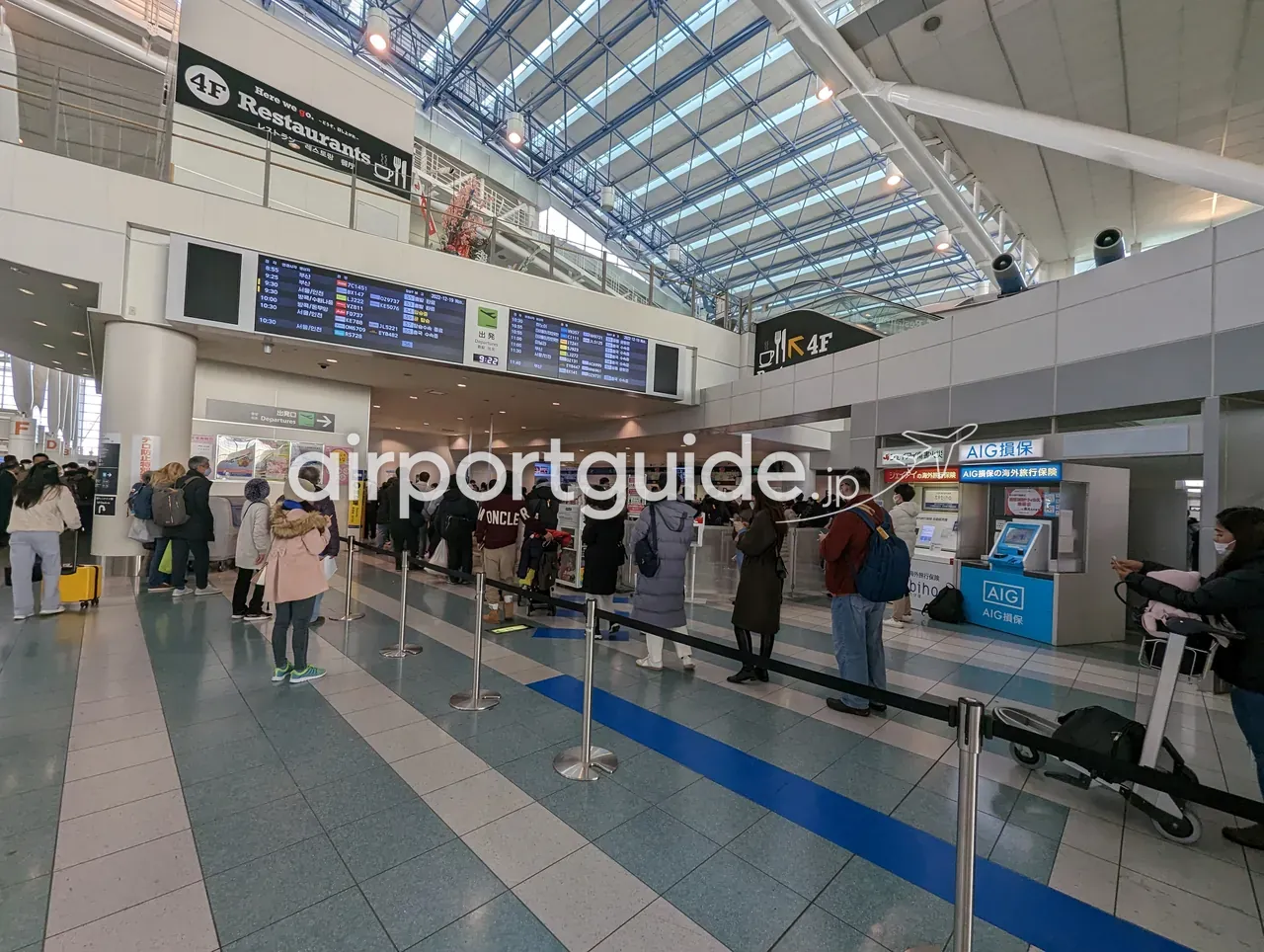 福岡空港国際線ターミナルの出発フロア。「4F Restaurants」のサインと出発便案内板（釜山・ソウル仁川・バンコクなど）が並び、「出発口 Departures」へ向かう旅客の列、右手にAIG損保・ジェイアイ傷害火災の海外旅行保険カウンター。