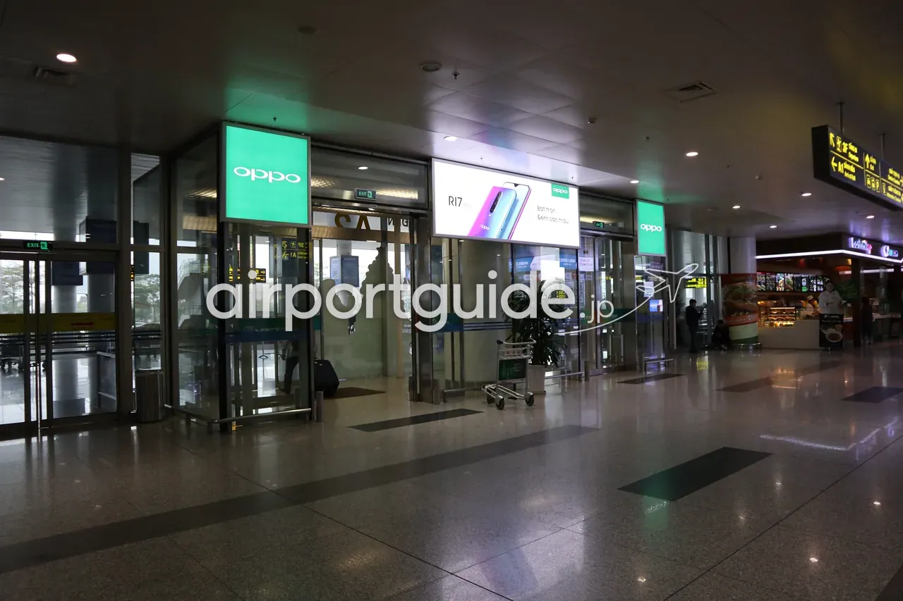 ノイバイ空港到着階の出口付近。緑色のOPPOストアのサインに挟まれた自動ドア「EXIT」、OPPO R17のベトナム語広告、右手に軽食店、手荷物カート。