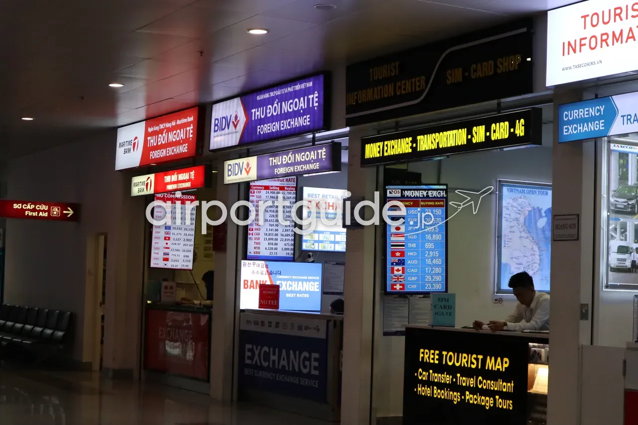 ノイバイ空港到着ロビーの外貨両替カウンター。「THU ĐỔI NGOẠI TỆ / FOREIGN EXCHANGE」の光る看板、各通貨のレート表示ボード、「MONEY EXCHANGE - TRANSPORTATION - SIM CARD - 4G」の帯、ベトナム地図を掲げたTASECOのブースと「FREE TOURIST MAP」。