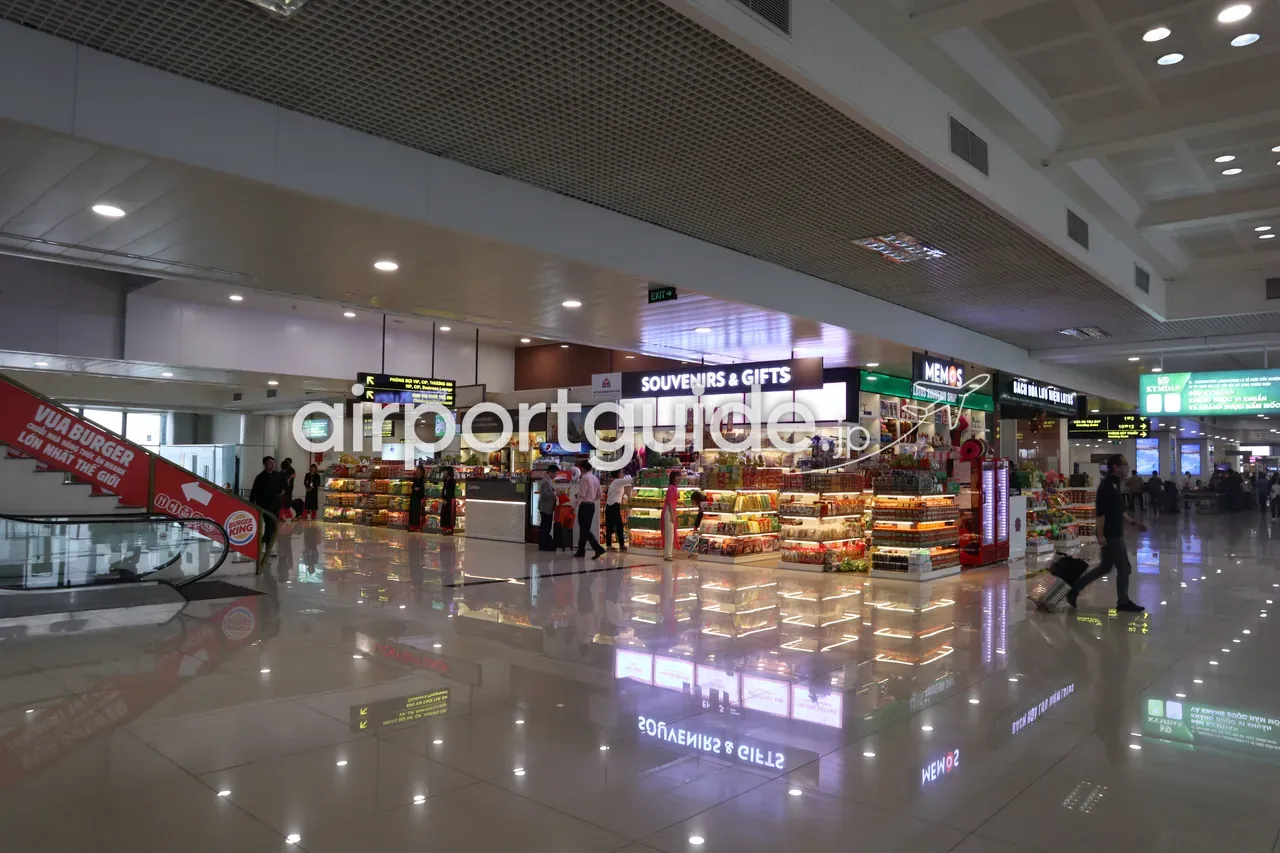 ノイバイ空港・国内線出発コンコースの物販エリア。「SOUVENIRS & GIFTS」「MEMOS」の店、エスカレーター脇の「VUA BURGER / BURGER KING」の案内、明るく積まれた菓子・土産の島型什器。