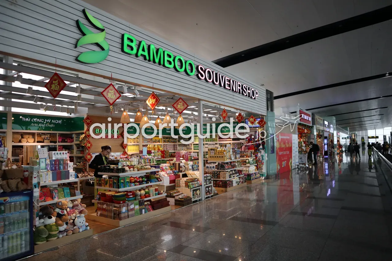ノイバイ空港制限エリアの「BAMBOO SOUVENIR SHOP」店頭。緑の竹のロゴ、旧正月の赤い「福」飾り、ベトナムコーヒー・緑茶・キャンディ・工芸品の棚、「Hà Nội Specialties（ハノイ名産）」の表示、Pepsiの冷蔵ケース、奥に「VIET NAM GIFT SHOP」。