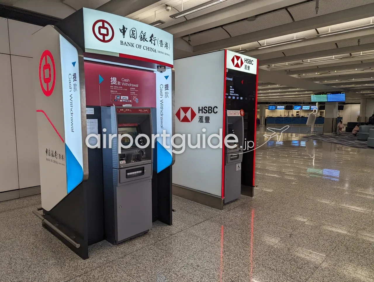 香港国際空港・到着エリアの中國銀行（香港）とHSBC（滙豐）のATM2台。『提款 Cash Withdrawal』の表示、奥に到着ホールのカウンター群。