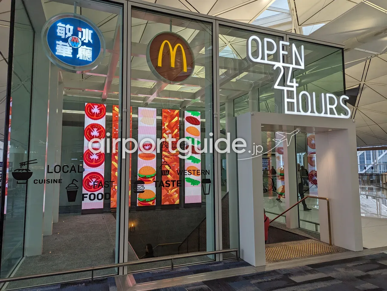 香港国際空港の24時間営業の飲食ゾーン入口。ガラス越しにマクドナルドのMマークと『敏華冰廳 MW』の看板、ネオンの『OPEN 24 HOURS』、床面に『LOCAL CUISINE / FAST FOOD / WESTERN TASTE』のピクトグラム、下階への階段。