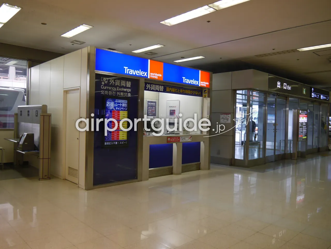 羽田空港の両替所「Travelex」のカウンター。青い看板と為替レートの表示板があり、右手に自動ドアの「出口 Exit」が見える。