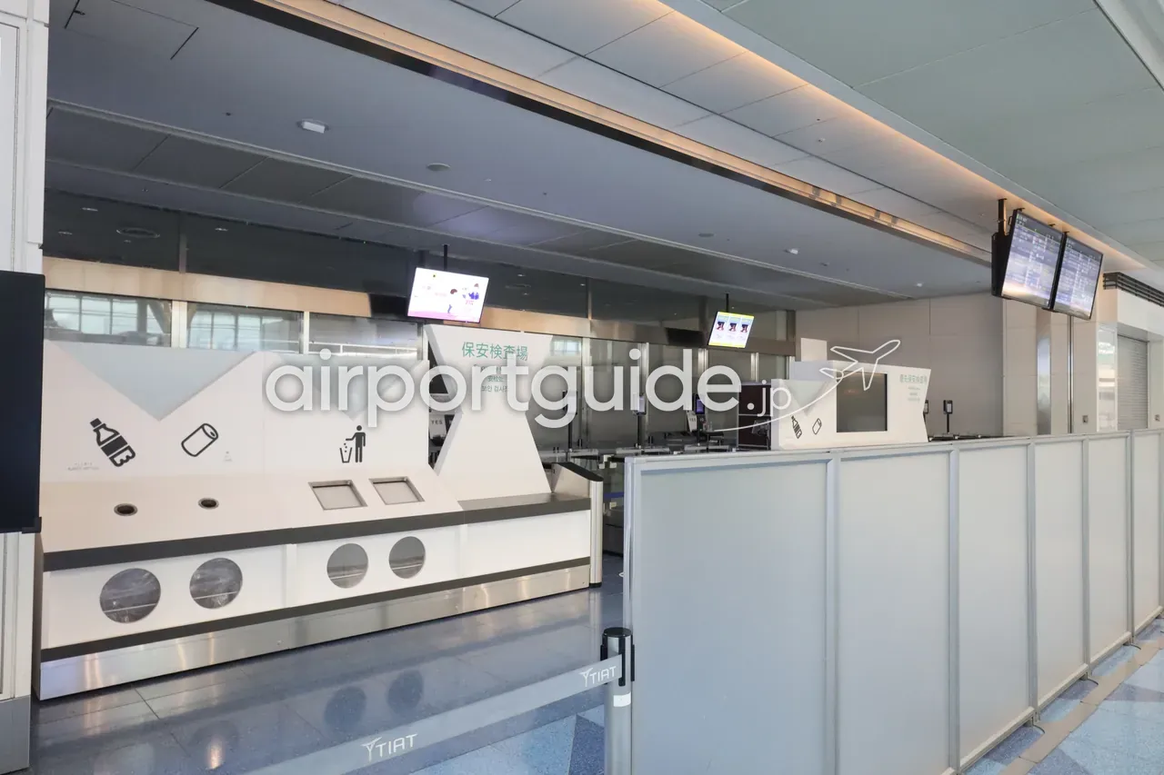 羽田空港第3ターミナルの保安検査場（Security Check）。手荷物トレーの投入台とX線検査レーン、液体物の廃棄ピクト。早朝で無人。