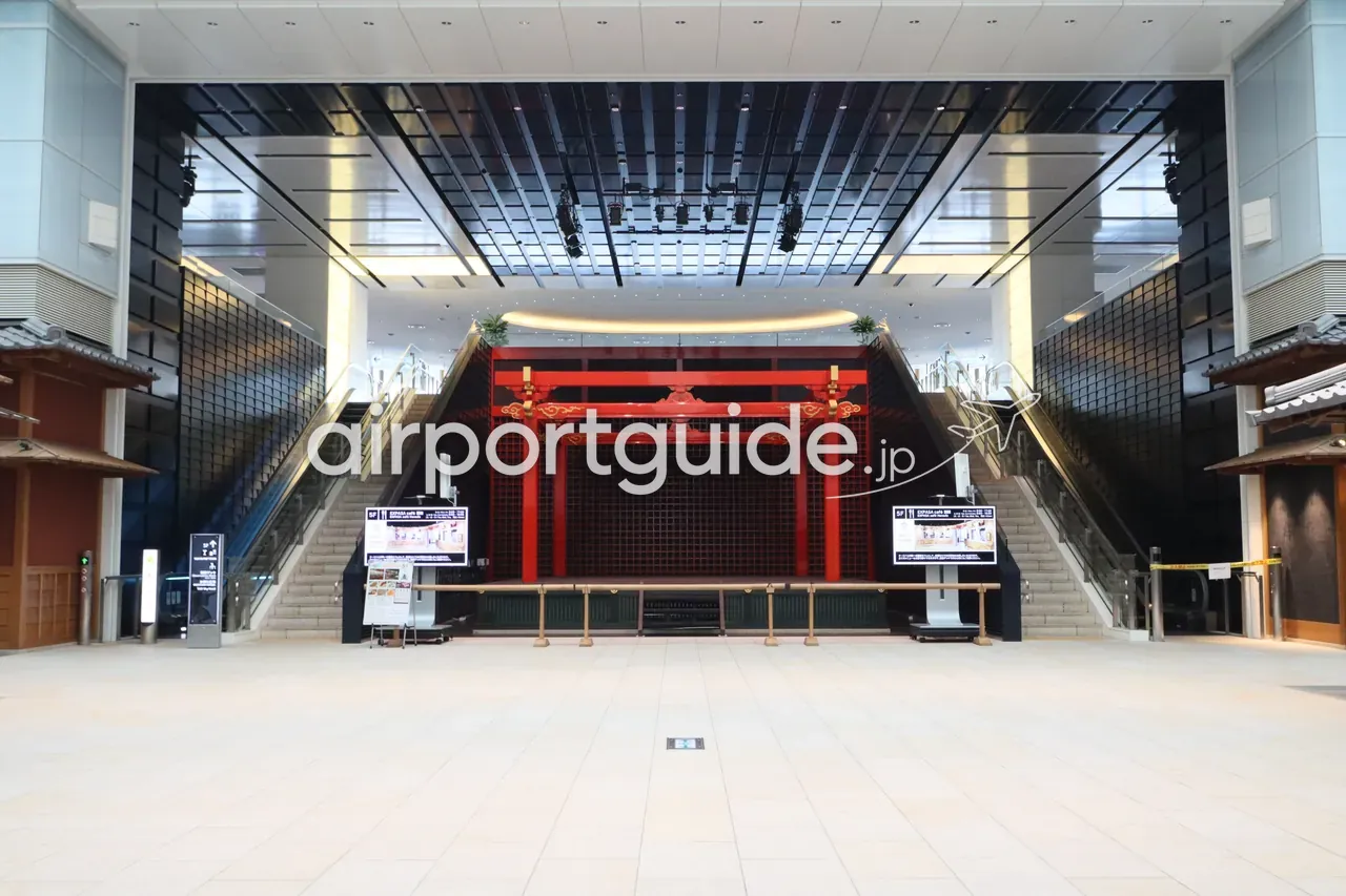 羽田空港第3ターミナル『江戸小路』のお祭り広場。中央に朱塗りの社殿風ステージ、左右へ上る対称の大階段、黒基調の装飾空間。