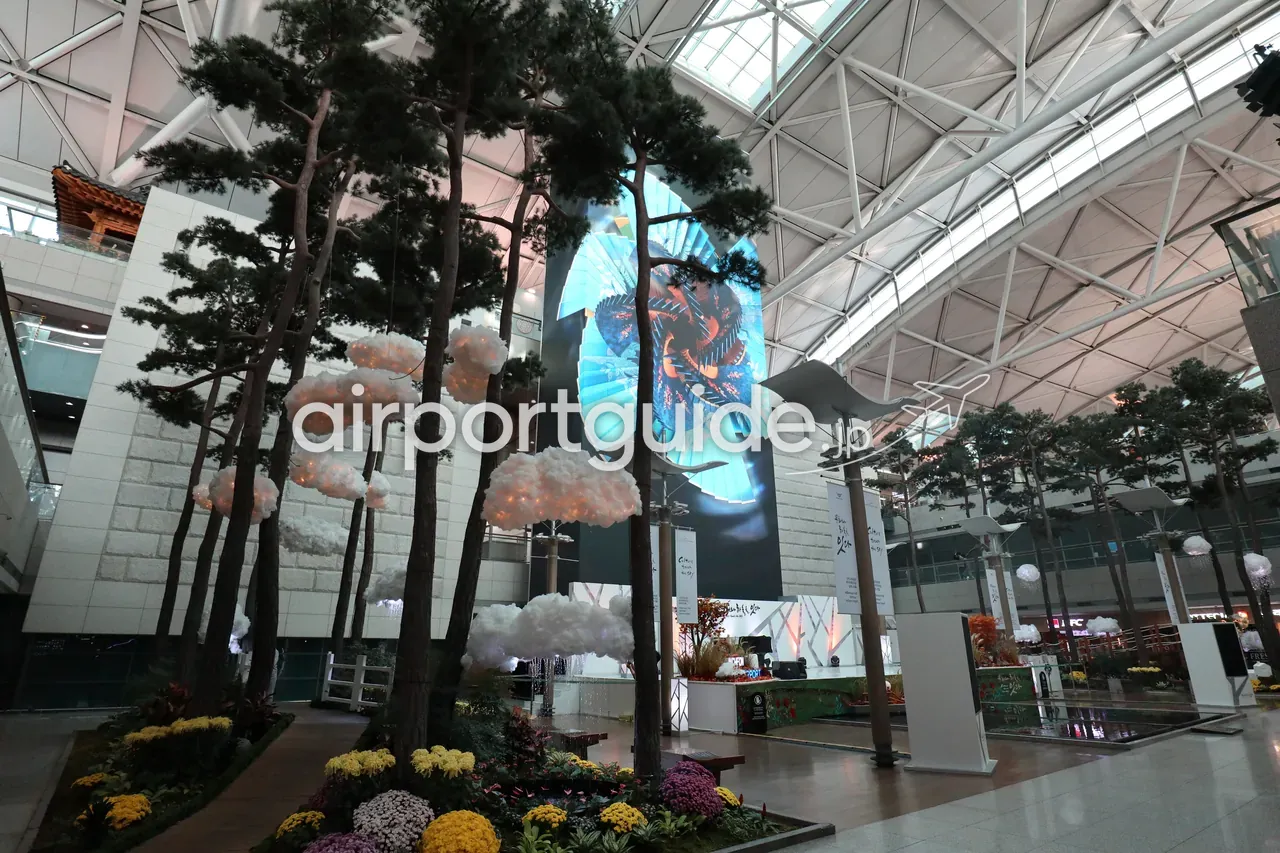 仁川空港の屋内庭園。本物の松の木立と吊り下げられた雲のオブジェ、韓国の伝統模様をあしらった大型メディアアートの壁、足元に色とりどりの花壇。