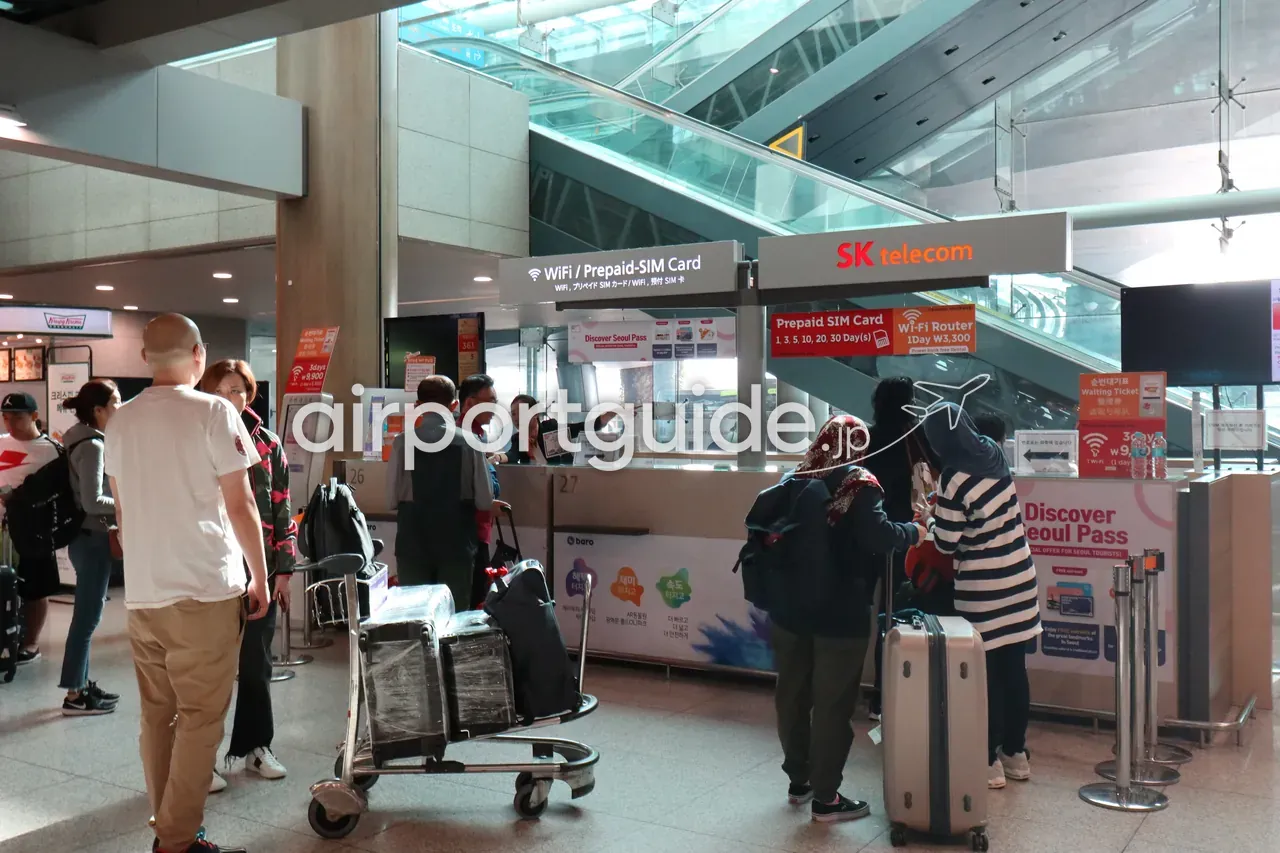 仁川空港到着階の通信カウンター。「WiFi / Prepaid-SIM Card」「SK telecom」のサインの下で、旅行者がプリペイドSIMやWi-Fiレンタルの手続きに並ぶ。
