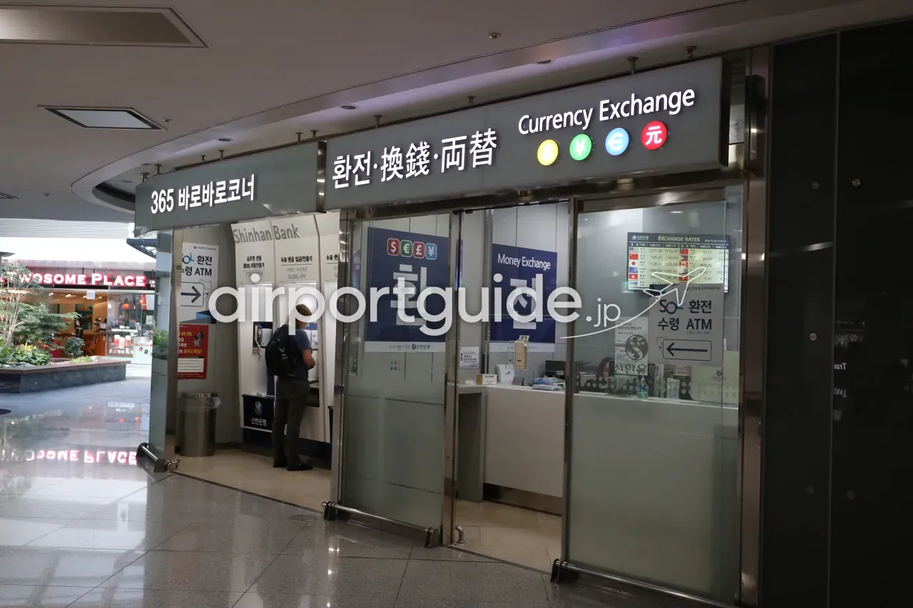 仁川空港の新韓銀行の外貨両替所と365 Global ATMコーナー。バックパックの男性がATMを操作している。