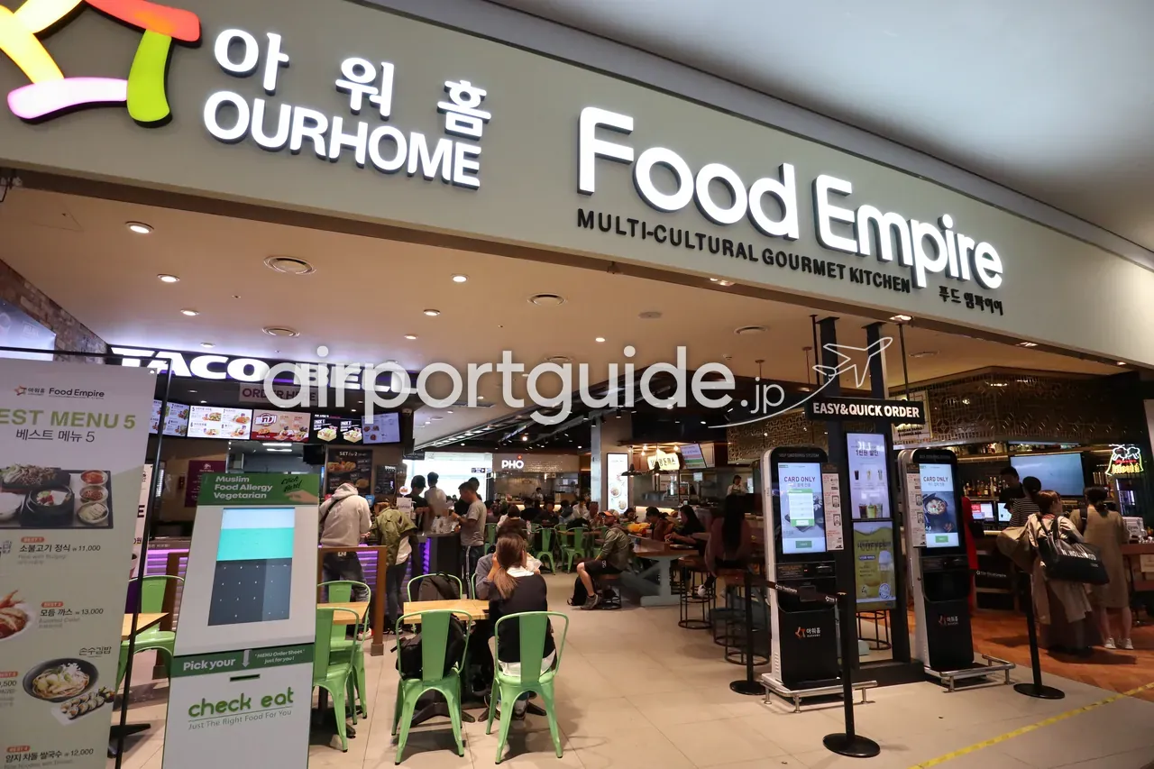 仁川空港のフードコート「아워홈 OURHOME Food Empire」。TACO BELLやPHOなど多国籍の店とセルフオーダー端末、席で食事をする人々。