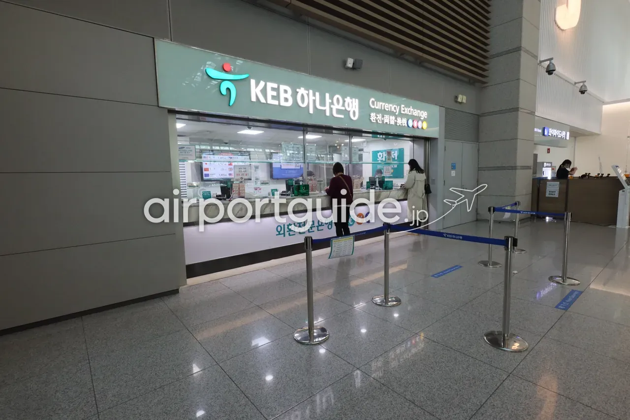 仁川空港のKEBハナ銀行 外貨両替カウンター。レート板の前で2人の客が両替の手続きをしている。