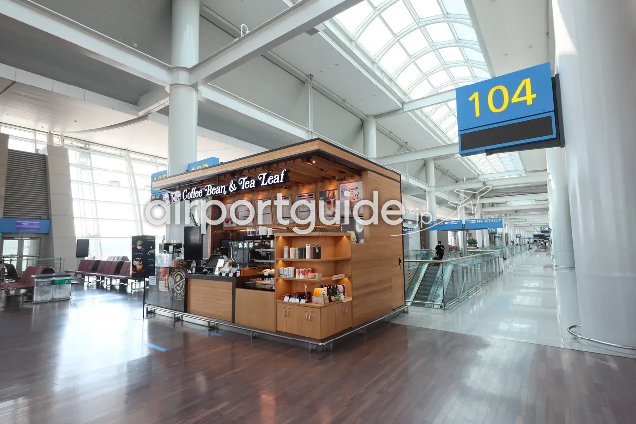 仁川空港の搭乗ゲート104近くの「The Coffee Bean & Tea Leaf」キオスク型カフェ。木製ブースにメニュー表とエスプレッソマシン、天窓の明るいコンコース。