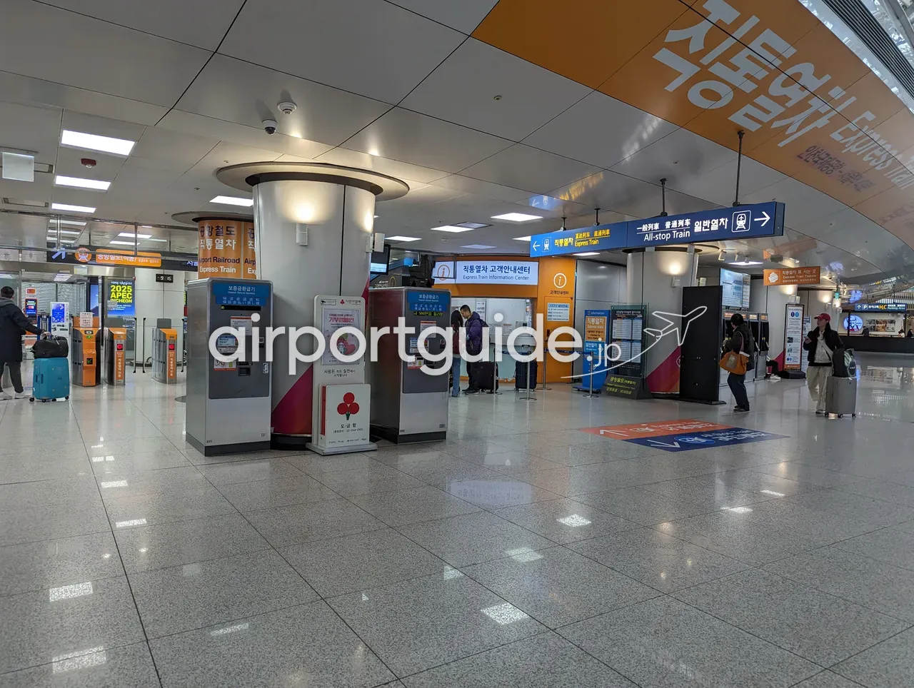 仁川空港のAREX（空港鉄道）駅コンコース。「직통열차 Express Train 直通列車」「일반열차 All-stop Train 一般列車」のオレンジと青の案内サイン、券売機、案内センターが並ぶ。