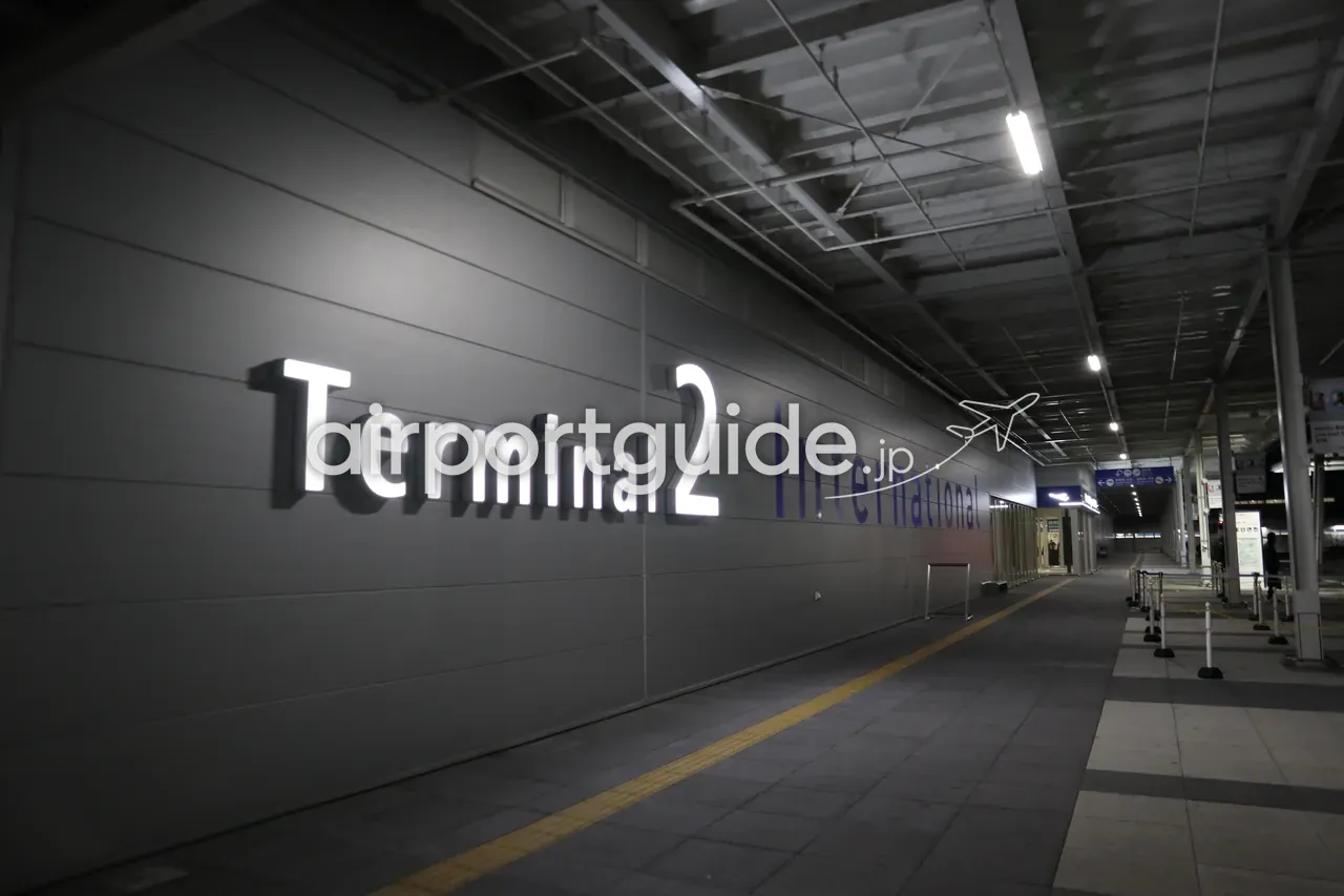 夜の関西空港第2ターミナルの外側。壁面に白と青のライトで「Terminal 2 International」の大きな文字が掲げられた連絡通路。