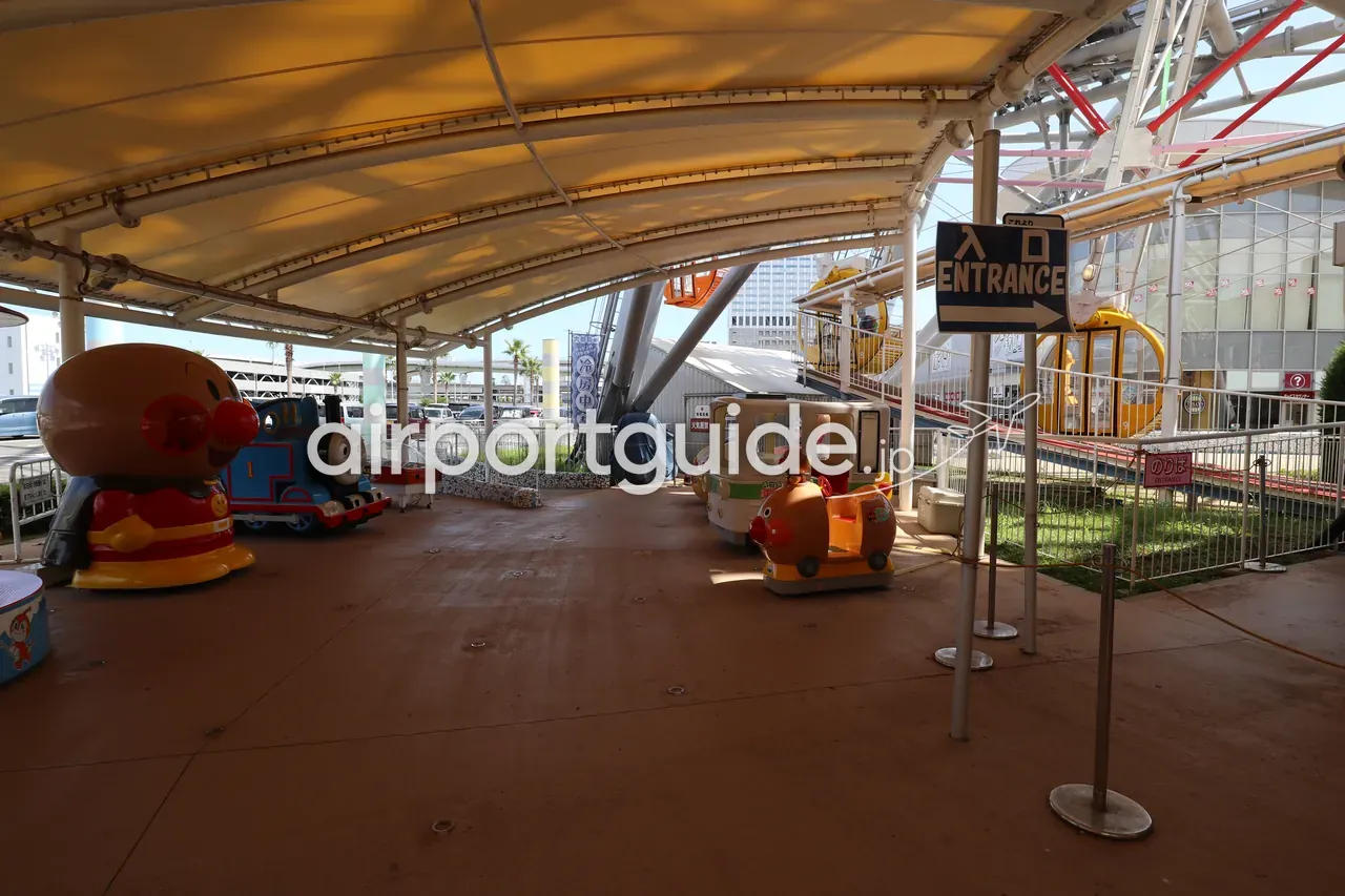 りんくうシークルの屋外キッズ遊具コーナー。アンパンマンやトーマスの乗り物と「入口 ENTRANCE」の案内、右手に観覧車の黄色いゴンドラ。