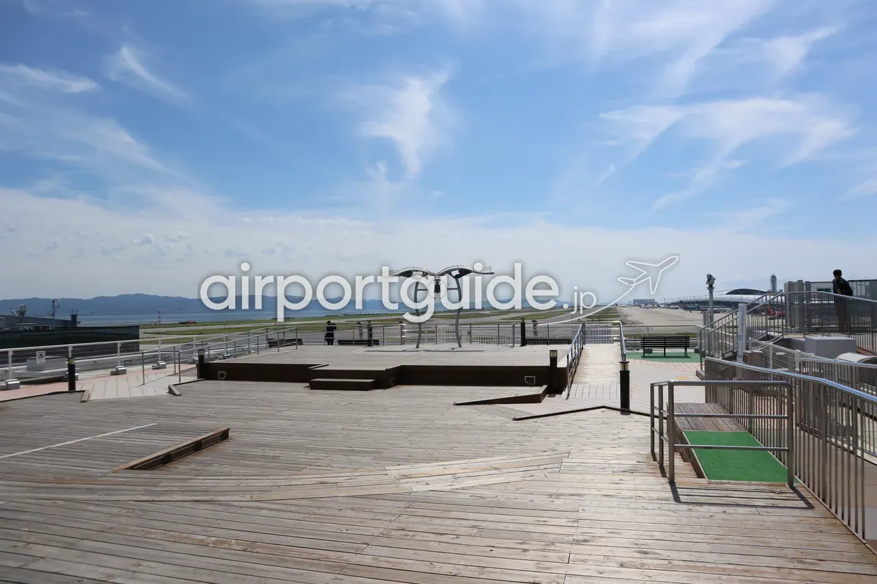 関空展望ホール スカイビューの屋上「スカイデッキ」。木張りのデッキの先に鐘のモニュメント、その奥に滑走路と大阪湾、晴れた空が広がる。