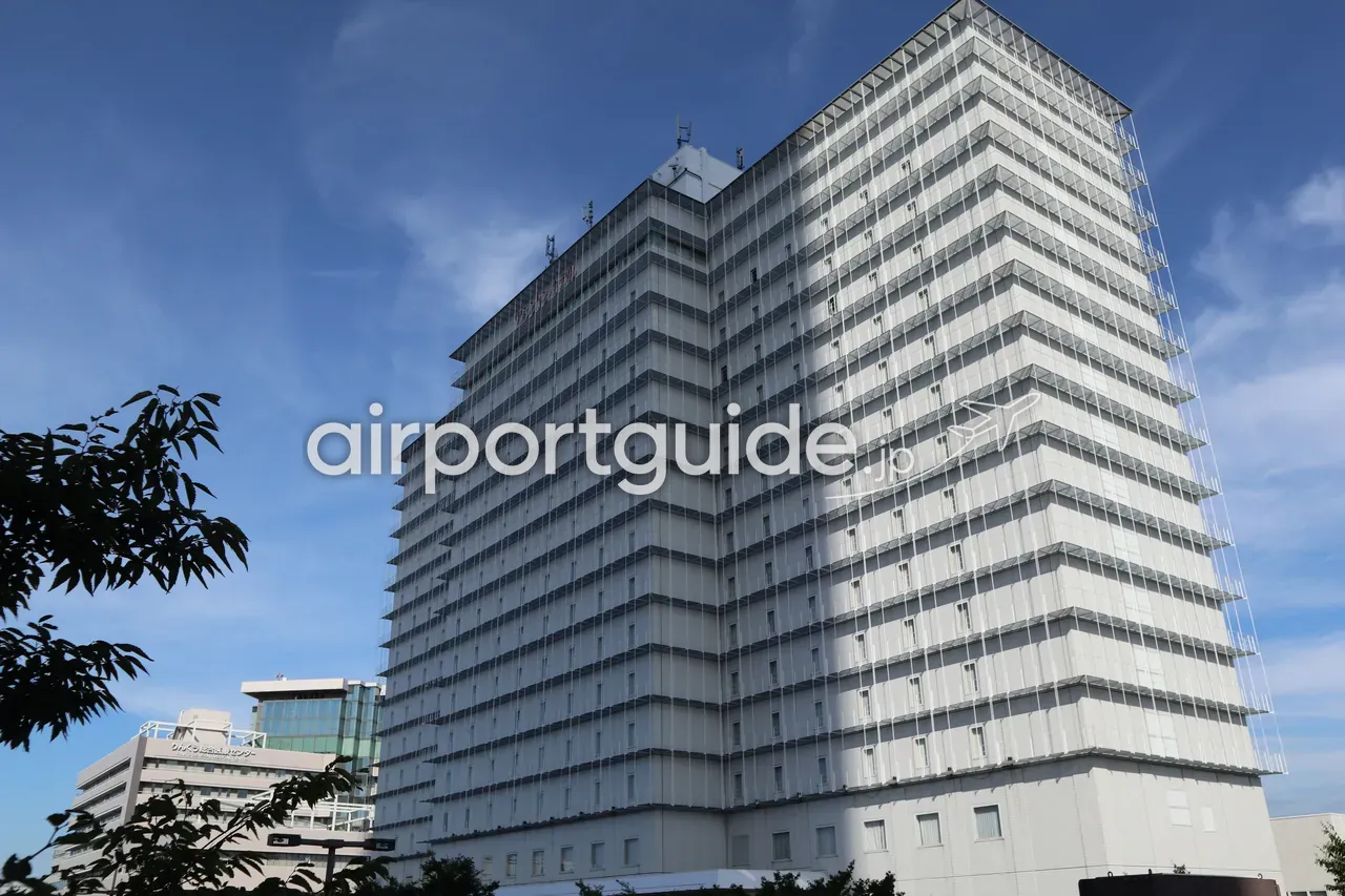 関西エアポートワシントンホテルの外観。青空の下、りんくうタウンに建つ白い高層の建物で、屋上にホテルのロゴ、手前に街路樹。