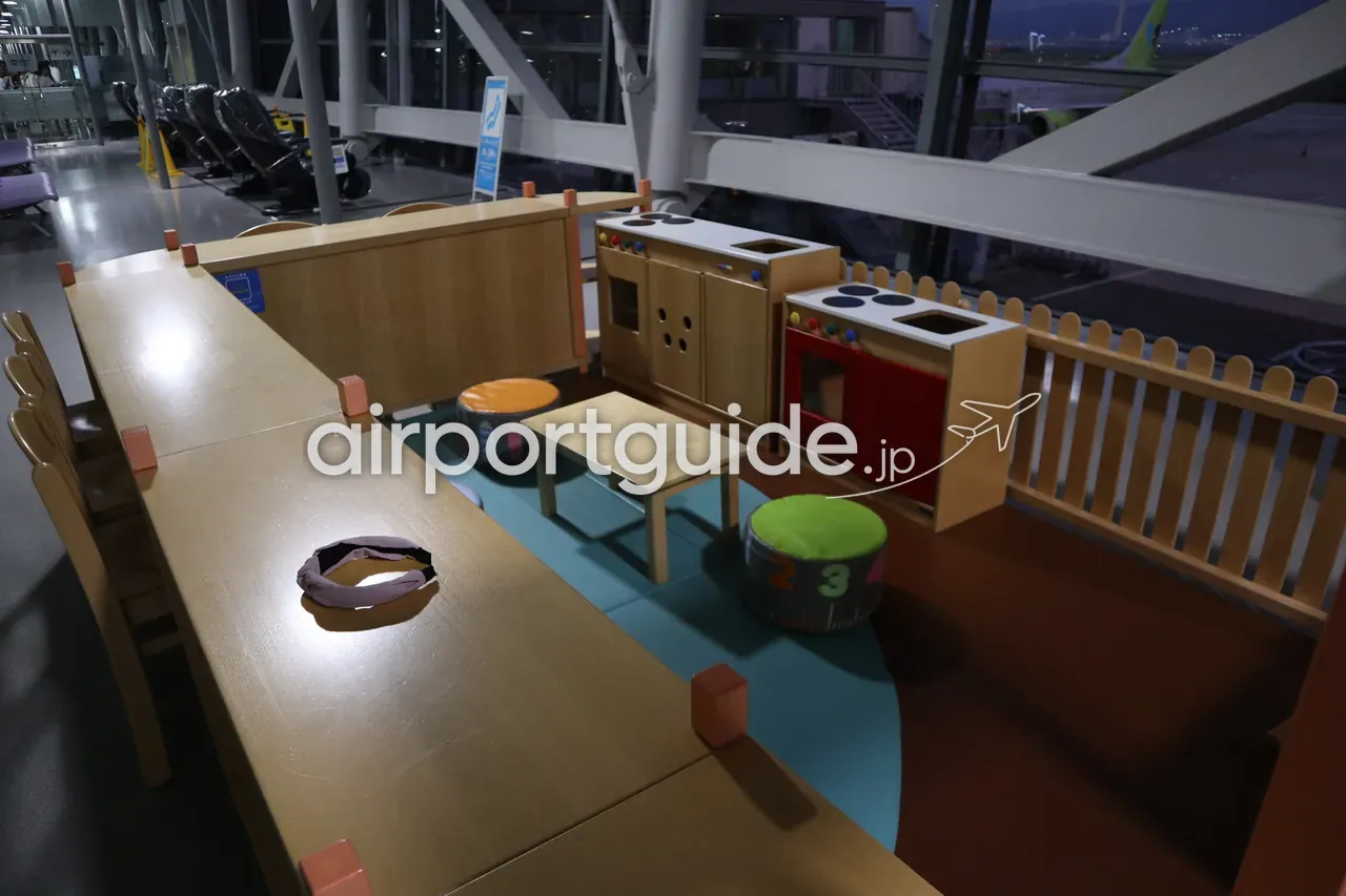 夜の関西空港ゲート付近のキッズコーナー。木製とレッドのおままごとキッチン、小さな机と椅子だけが置かれ、窓の外にスクート機。
