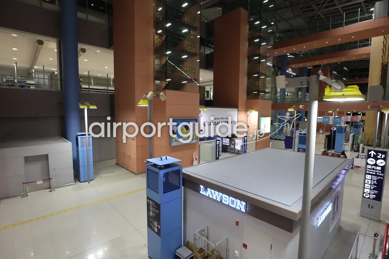 関西空港ターミナルの吹き抜けロビー。「KANSAI AIRPORTS」の看板とコンビニ「LAWSON」のキオスク、「国内線 Domestic ↑2F」などの案内標識が見える。