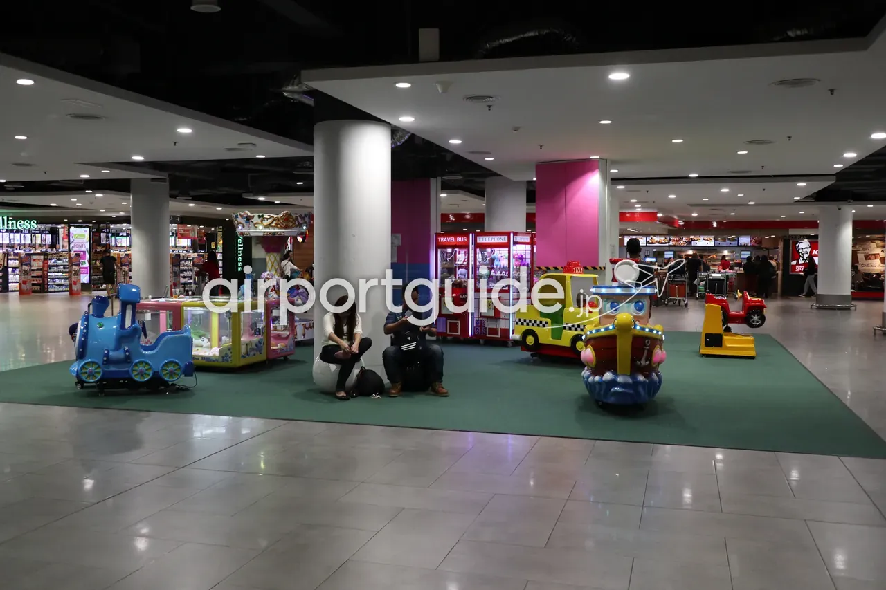 gateway@klia2のモール内、子ども向けのコイン式乗り物コーナー。緑のマットの上に電車・タクシー・ボートを模した乗り物が並び、奥にKFC。