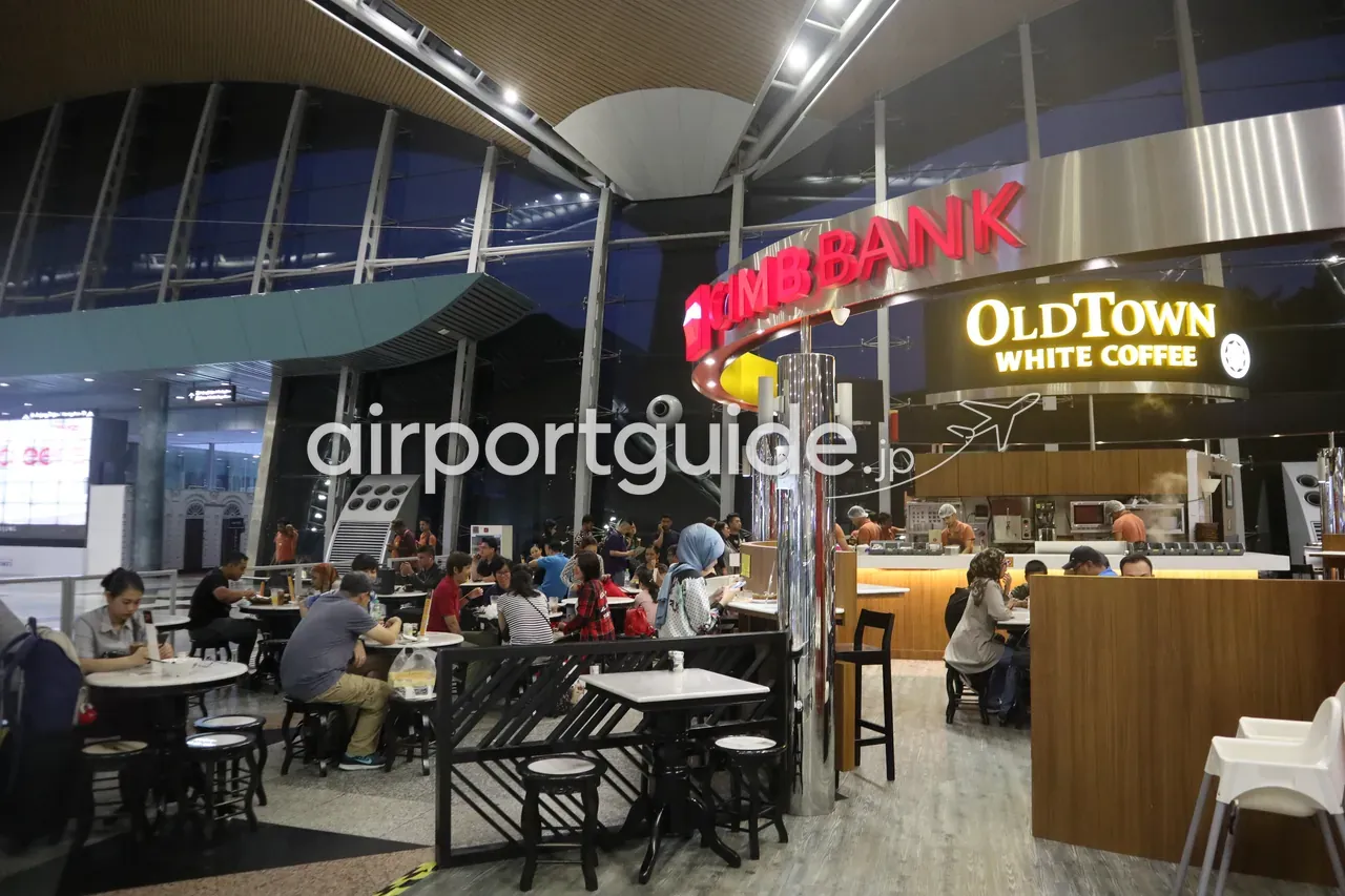 KLIAターミナル1の「OldTown White Coffee」と混み合うイートインエリア。CIMB Bankの看板の隣に木目調のカウンター、波打つ大屋根の下でテーブル席が埋まっている。