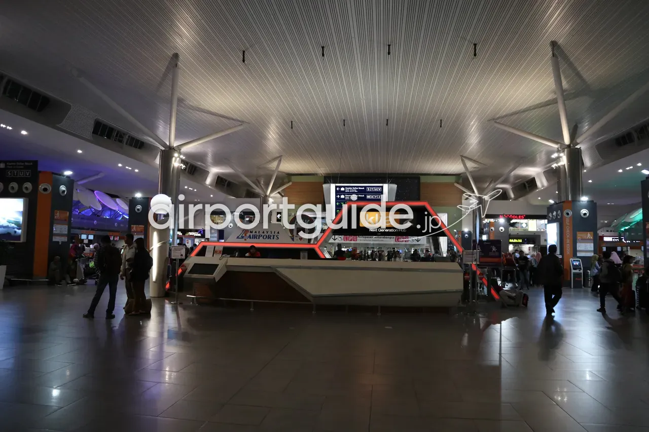 ターミナル2の中央インフォメーションデスク「klia2 Next Generation Hub」。傘状に開いた白い支柱と天井の下に「ASK」の案内カウンター、両側にチェックインカウンターやNOODLESの店。