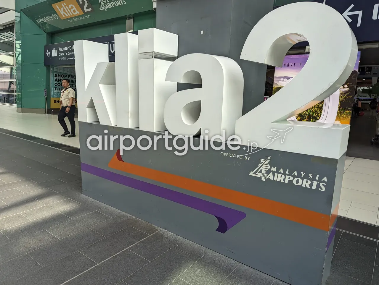 ターミナル2の立体ロゴモニュメント。白い大きな「klia2」の文字と、台座の「OPERATED BY MALAYSIA AIRPORTS」の表示、背後に「Welcome to klia2 Next Generation Hub」の入口サイン。