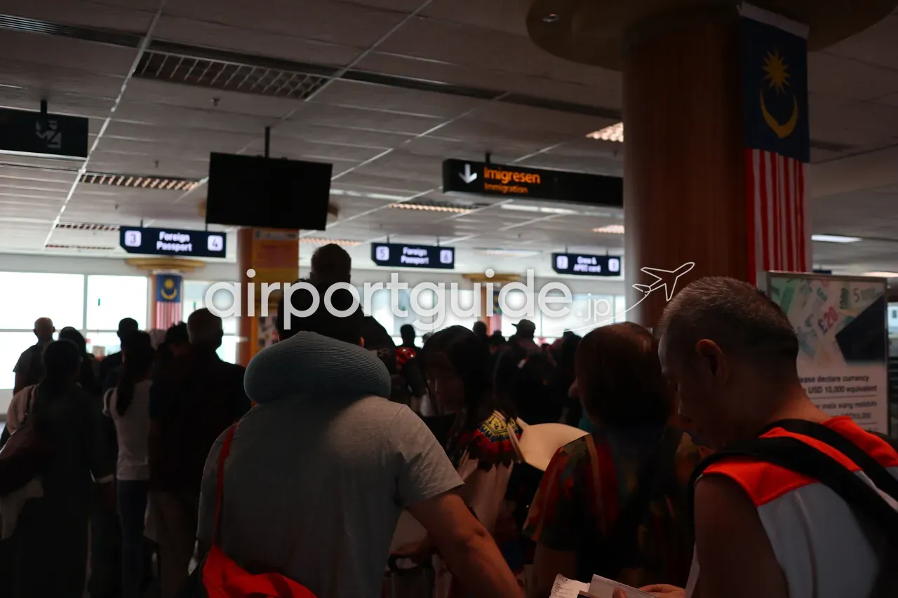 ランカウイ国際空港の入国審査ホール。『Imigresen / Immigration』の吊り看板と『Foreign Passport』カウンター案内（3・5・6番）、天井から下がるマレーシア国旗、審査を待つ大勢の旅客の列。