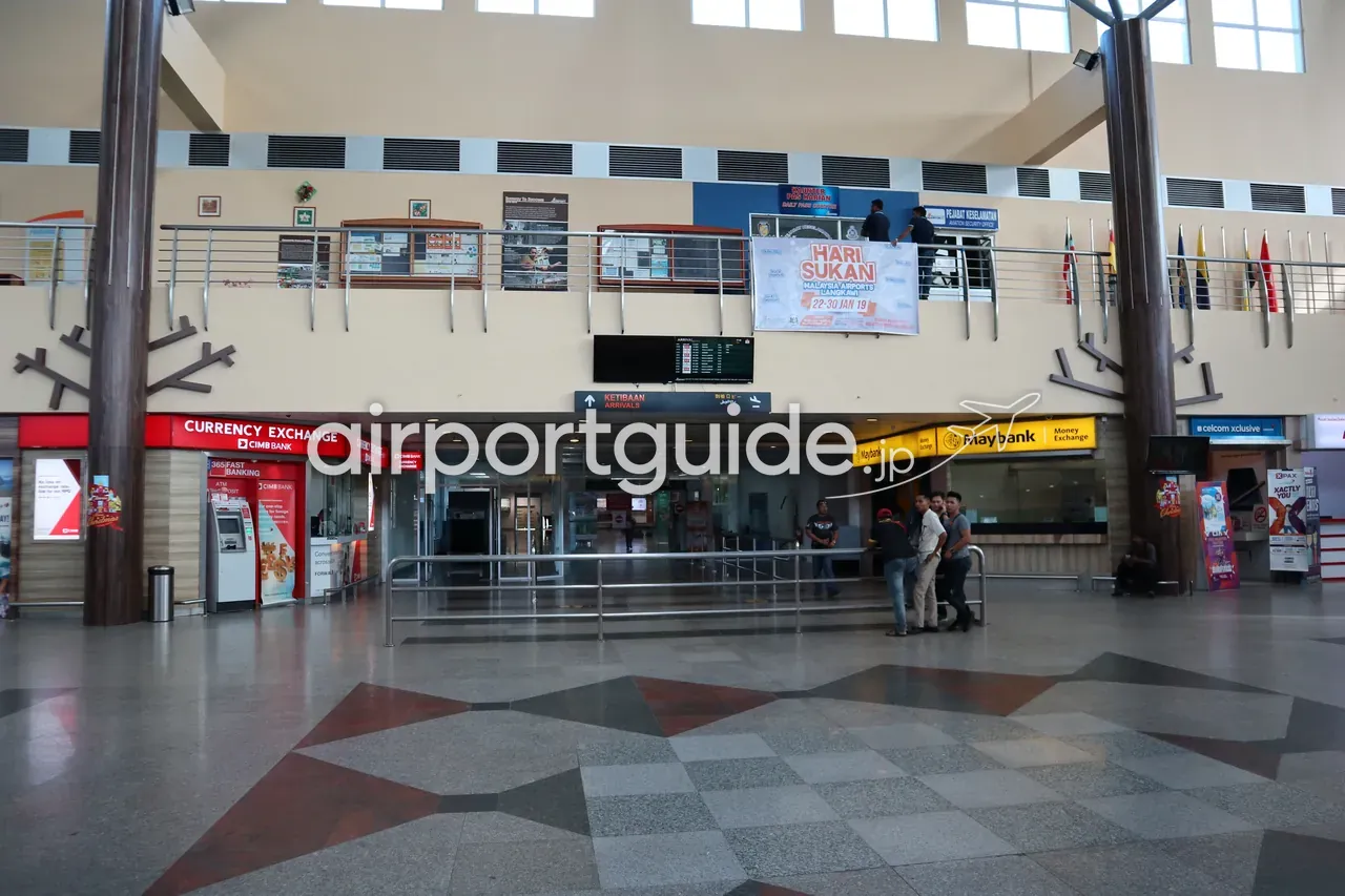 ランカウイ国際空港の到着ホール下部。左に赤い『CURRENCY EXCHANGE CIMB BANK』の両替カウンターとATM、右に黄色い『Maybank Money Exchange』、中央に『KETIBAAN ARRIVALS』の案内、星型模様の石の床。