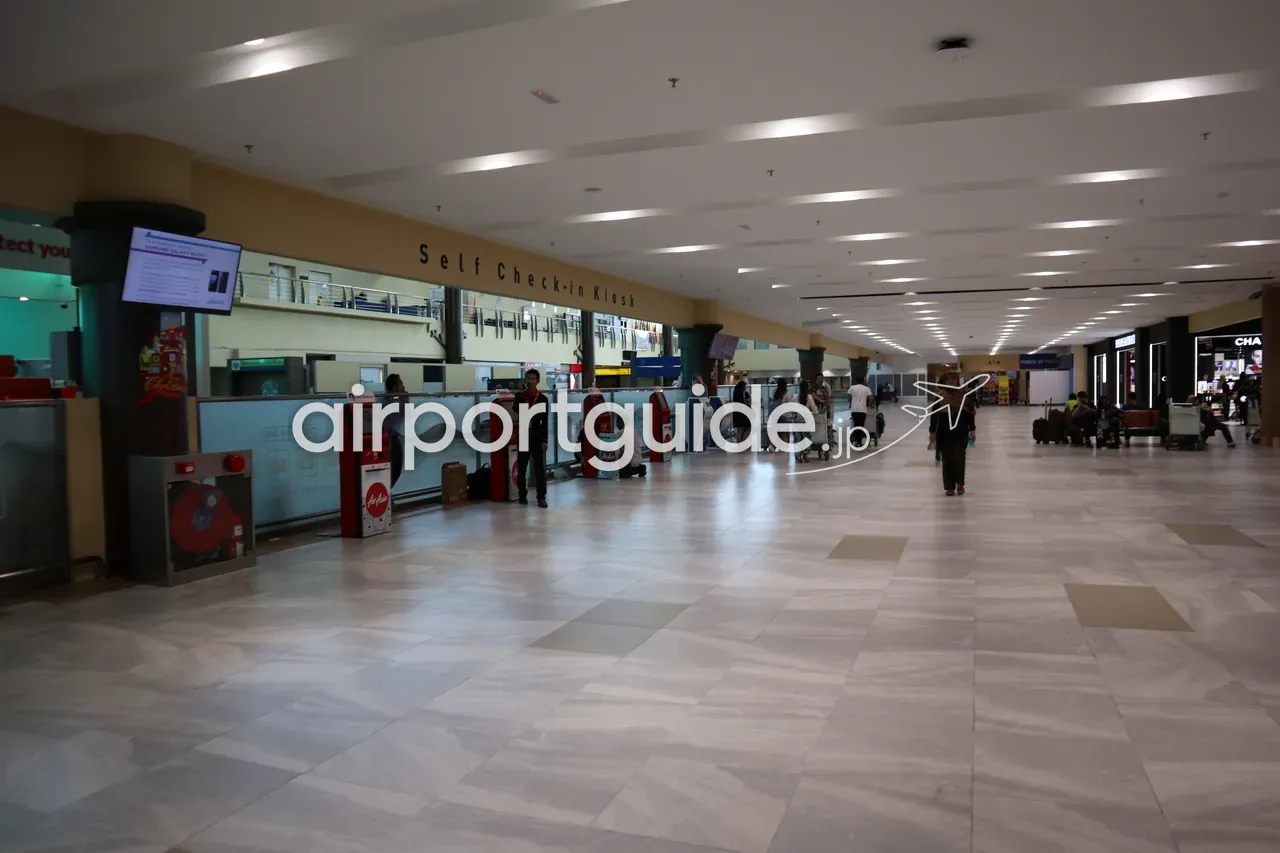 ランカウイ国際空港のチェックインエリア。壁上部に金色の『Self Check-in Kiosk』の表示、AirAsiaの赤いセルフチェックイン機が一列に並び、大理石調の床、右奥にCHANELの店。
