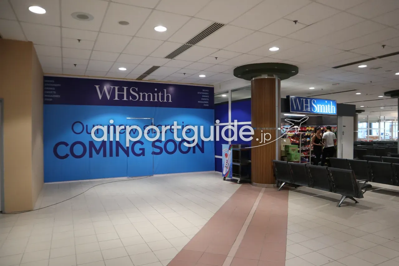 ランカウイ国際空港の制限エリアにある売店『WHSmith』。青い店構えに『WHSmith SNACKS』の看板、隣に『Our new store is COMING SOON』の仮囲い、手前に連結ベンチ。