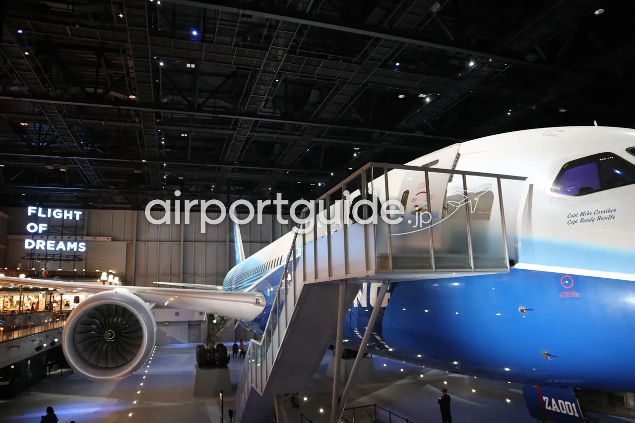 中部国際空港の商業施設「FLIGHT OF DREAMS」に展示された実機ボーイング787初号機（ZA001）。暗い館内に青と白の787、ガラス張りの搭乗ブリッジ、大型エンジン、左奥に「FLIGHT OF DREAMS」の照明サイン。