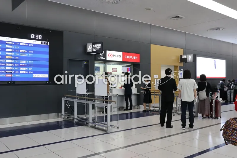 中部国際空港のMUFG（三菱UFJ銀行）外貨両替窓口に並ぶ旅行客の列。左に出発案内モニター。