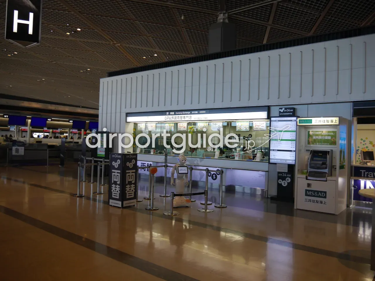 成田空港のGPA外貨両替専門店（世界34通貨対応）。窓口前に「両替 Currency Exchange」のサインと案内ロボット、右手にATM、奥にチェックインカウンター。