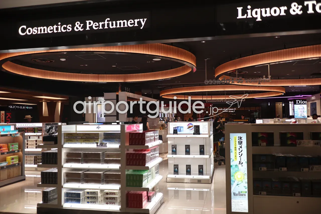 成田空港制限エリアの免税店。「Cosmetics & Perfumery」「Liquor & Tobacco」の照明サインの下に、化粧品ブランドカウンターとたばこの陳列棚。