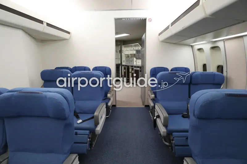 航空科学博物館の客室モックアップ内部。青いシートの間の通路の先に、機内ギャレー（厨房）設備が見える。