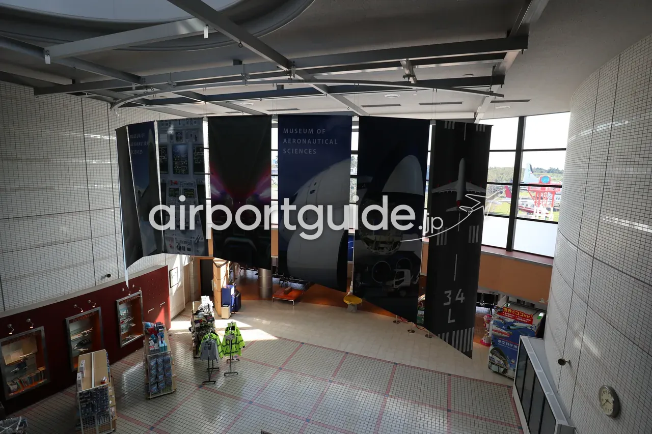 航空科学博物館のエントランスホールを2階から見下ろした様子。「MUSEUM OF AERONAUTICAL SCIENCES」の大きなタペストリーが吊られ、下階に売店や模型ケース。