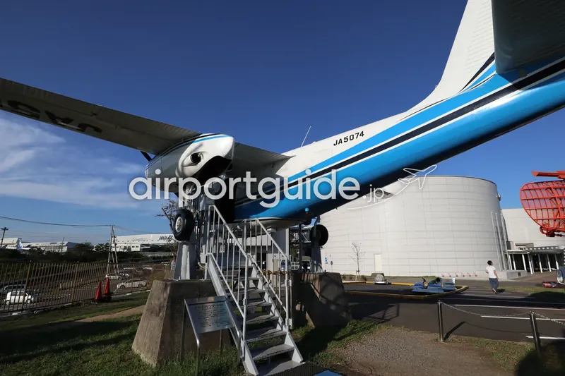 航空科学博物館の屋外展示、エアロコマンダー680高翼機。機体下から見上げるアングルで、奥に博物館本館。