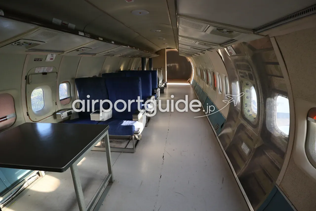 屋外展示された退役旅客機の機内キャビン。青いシート列と通路、丸い客室窓が残る往年の旅客機の内部。