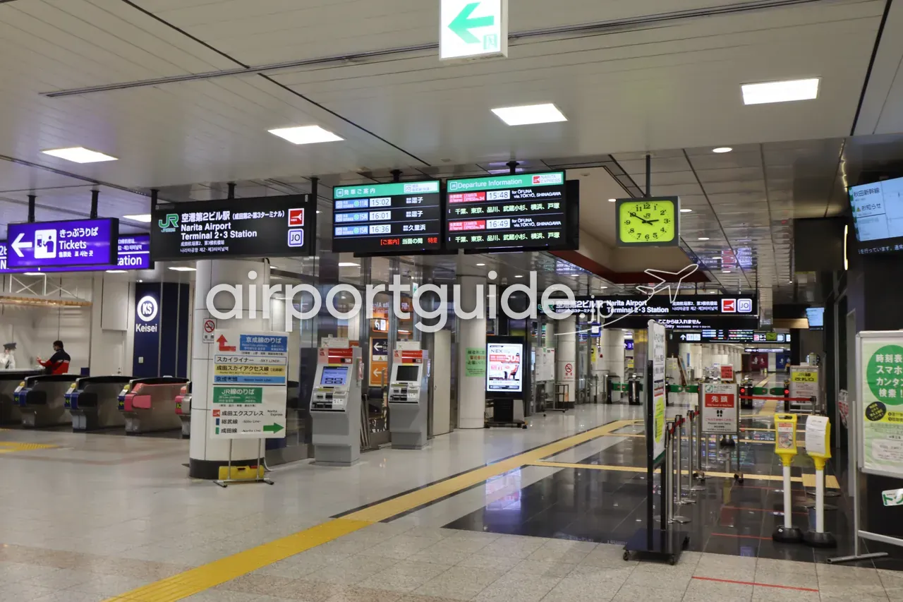 空港第2ビル駅（Narita Airport Terminal 2·3 Station）のコンコース。JR・京成の改札、京成スカイライナーとJR成田エクスプレスの案内、発車案内表示が並ぶ。